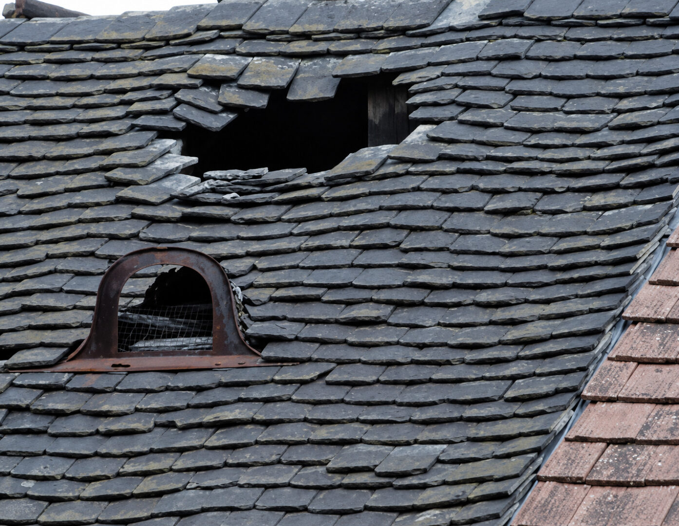 Severely damaged slate roof with missing and displaced tiles exposing a large opening in the roofing system