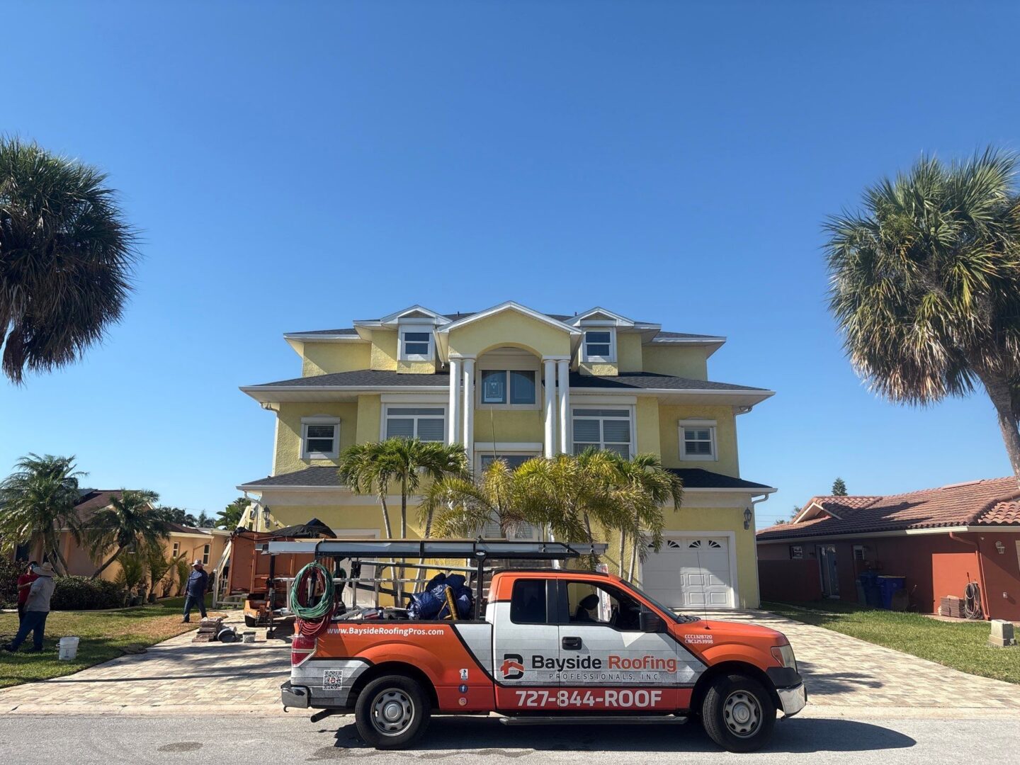 Bayside Roofing service truck parked in front of a yellow three-story home during a roofing project.